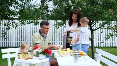 幸福美丽的家庭，妈妈，爸爸，四岁的儿子和一岁的女儿做新鲜果汁。 在夏天，在